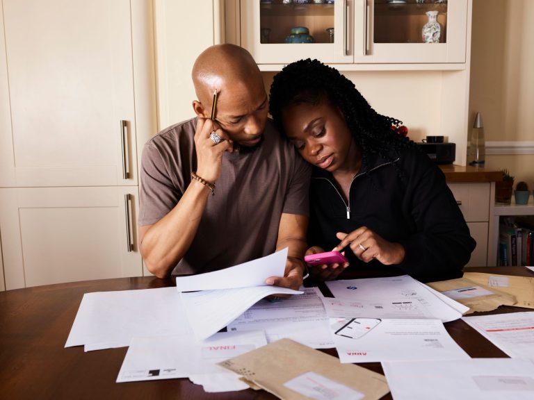 Casal organiza documentos e finanças domésticas enquanto usa um celular à mesa.