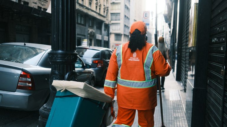 Trabalhador da limpeza urbana carrega equipamentos por uma rua de São Paulo.
