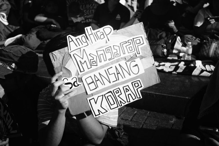 Participação cidadã pode orientar o desenho do Fórum SIMORE Brasil Pessoa segura um cartaz de protesto diante de um grupo de manifestantes.